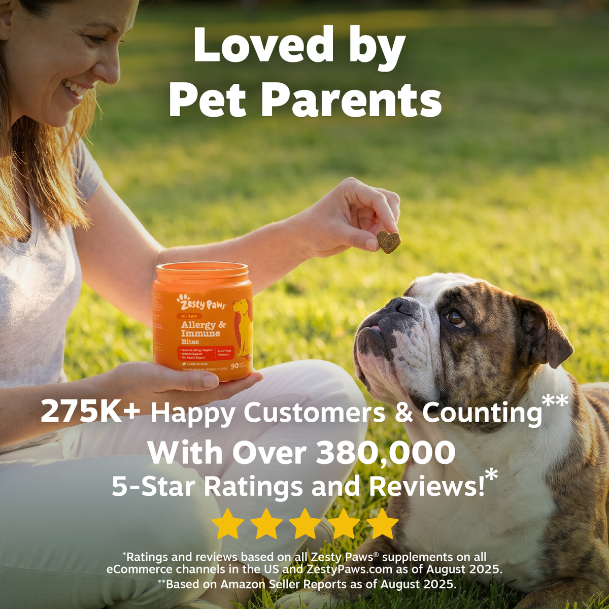 Woman holding orange jar of dog treats over a bulldog sitting on grass outdoors.